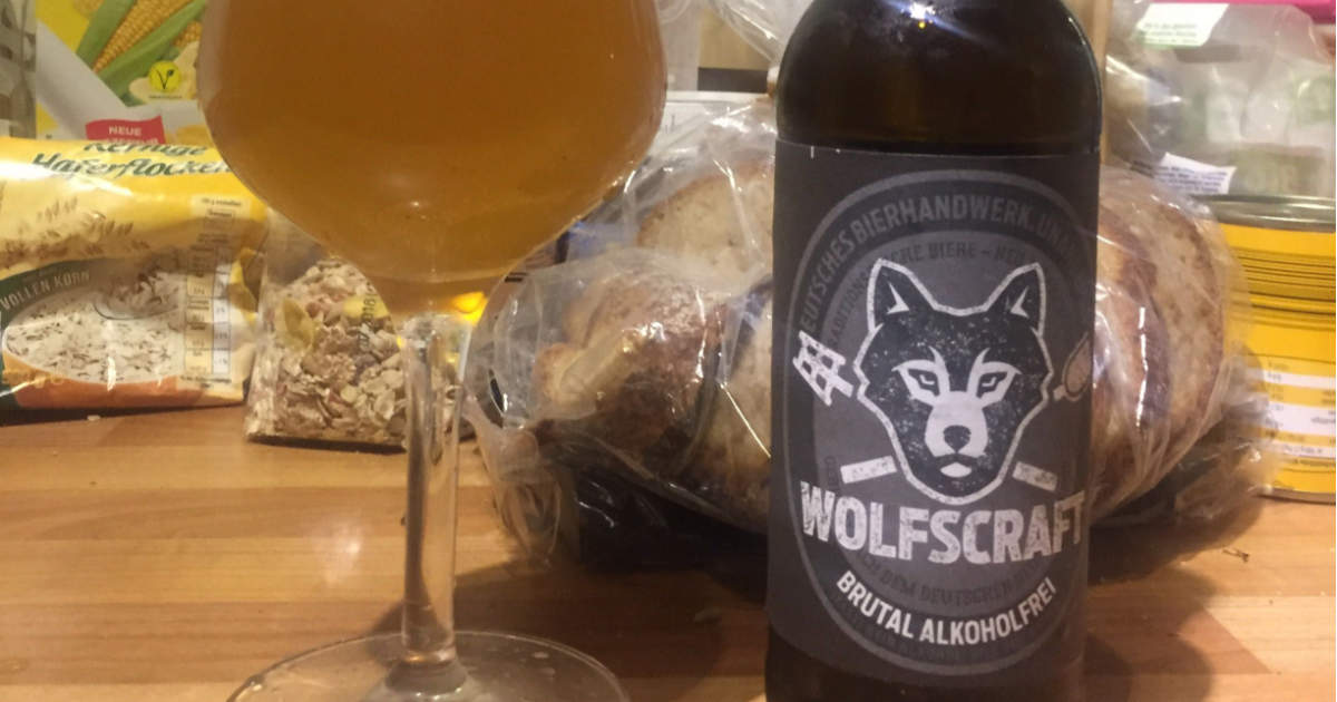 Dunkeloranges Bier mit viel Schaum in einem bauchigen Glas, auf der Flasche ist ein Wolf zu sehen